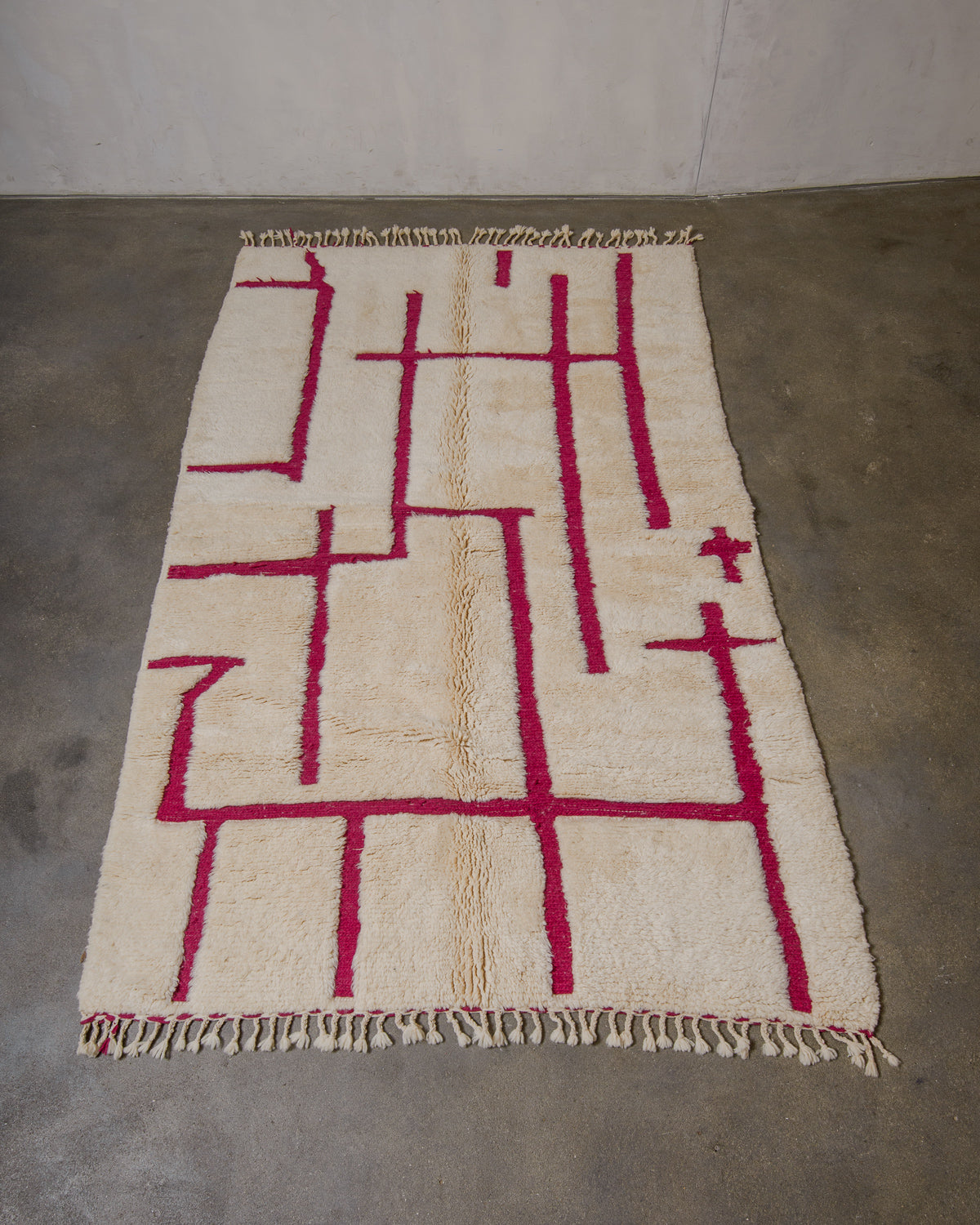 Cream and magenta geometric patterned rug on a concrete floor.